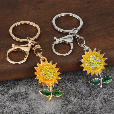 Gold-tone and silver-tone sunflower keychains displayed side by side on a wooden surface.