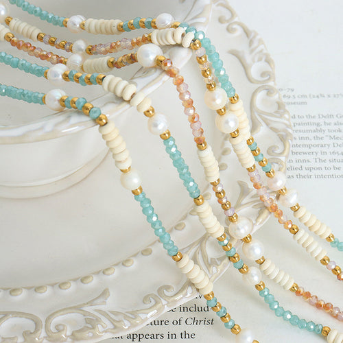 Pink and teal pearl bead necklaces draped on ornate white plate