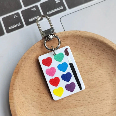 White acrylic heart paint palette keychain with silver lobster clip on wooden dish
