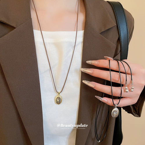 A brown cord necklace with small gold-tone beads and a textured oval pendant, styled view