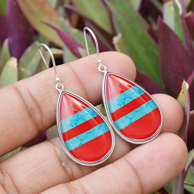 Red turquoise striped teardrop drop earrings held in hand over purple leaves
