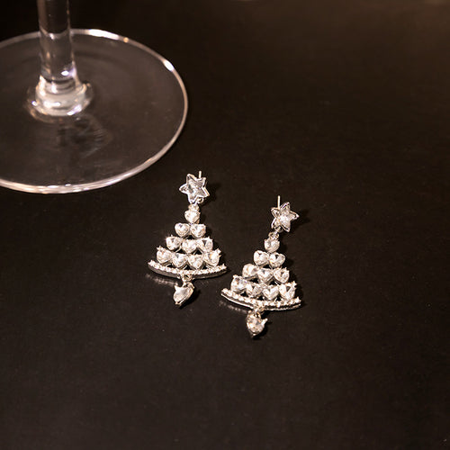 Silver crystal Christmas tree drop earrings on black surface near glass stem