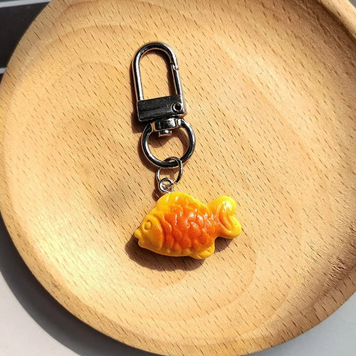 Yellow orange resin taiyaki fish keychain with silver lobster clip on wood dish