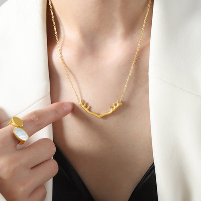 Model wearing gold antler V pendant necklace with finger pointing