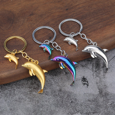 Gold, silver, and rainbow double dolphin keychains arranged on a wooden surface.