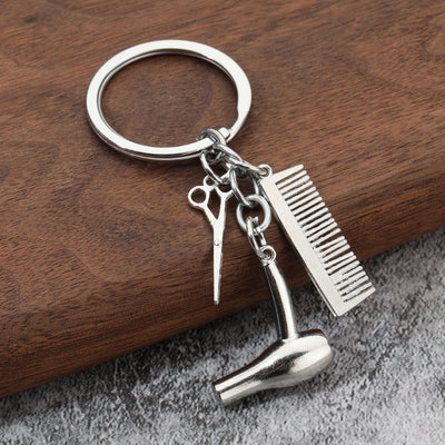 Close-up of silver-tone scissors, comb, and hair dryer charms on a wood surface.