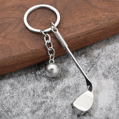 Silver-tone golf club and textured ball charms on a split ring over wood and gray fabric.