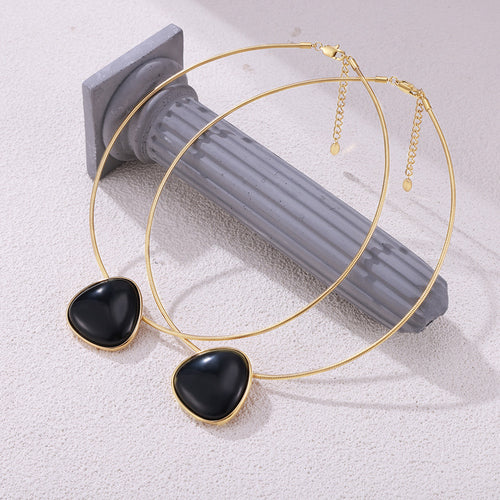 Two gold snake chain black triangle pendants styled on gray column prop