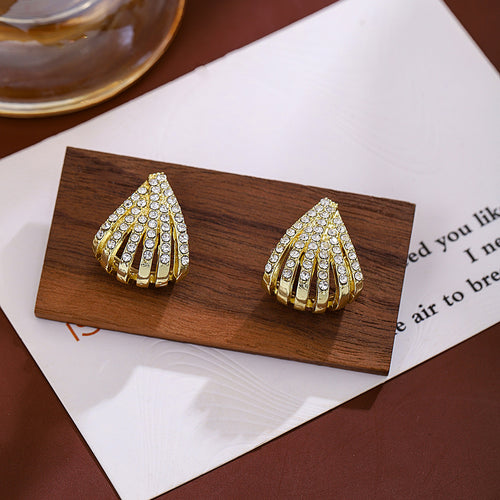 Gold fan rhinestone stud earrings on wood block over printed paper