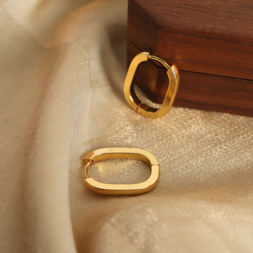 Two gold oval huggie hoops on gold fabric near wood box