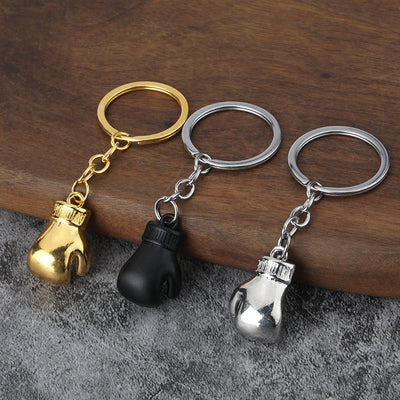 Three boxing glove keychains in gold tone, black, and silver on a wooden surface.