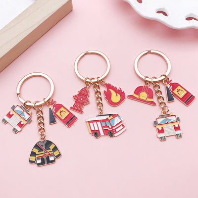 Three firefighter keychains arranged on a pink surface with colorful firefighting charms.