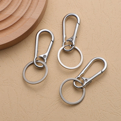 Three silver-tone clip keychains with circular split rings on a textured beige surface.