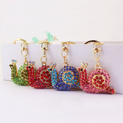Four green, red, blue, and pink stone-covered snail keychains arranged together.
