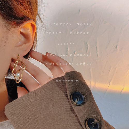 Gold-tone irregular-double-loop pearl asymmetric studs shown worn on an ear.