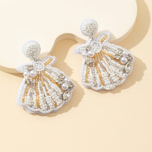 Beaded seashell earrings shown at an angle on cream background with beige dish