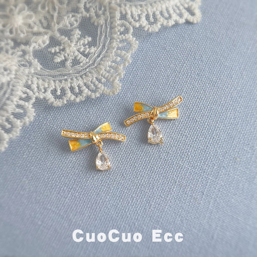 Gold-tone clear-stone ribbon bow and teardrop studs on blue fabric.