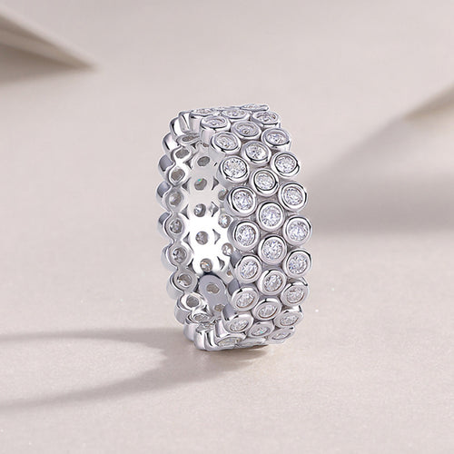 Silver three-row bezel-set round CZ band ring standing upright on beige fabric