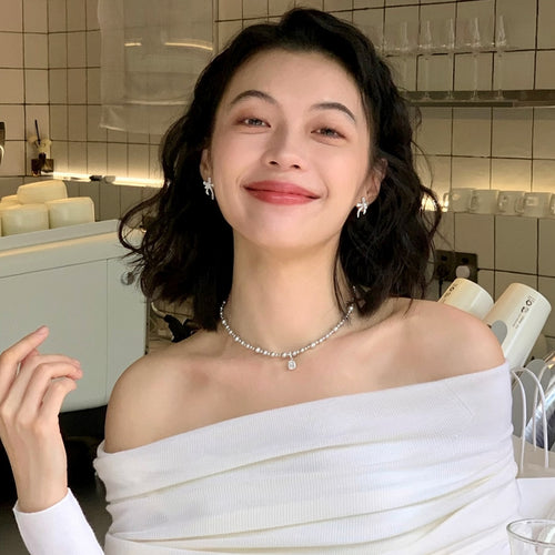 Styled wear view of 银色蝴蝶结珍珠耳钉 showing silver-tone bow tops, white pearl accents, and curved ribbon-like drops