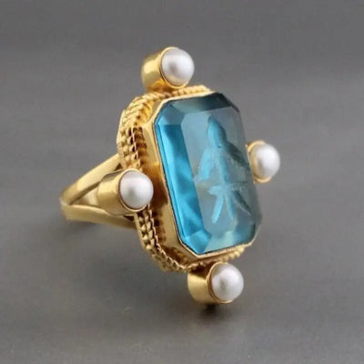 Angled gold ring blue gem four pearl accents on gray background