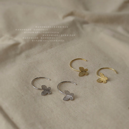 Gold and silver frosted butterfly hook earrings on beige fabric