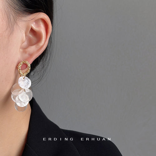 Gold-tone textured-oval translucent-white-disc tassel earrings shown worn on an ear.