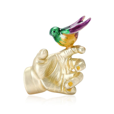 Front view of small colorful bird perched on a sculpted hand with a pearl-like accent