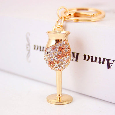 Gold-tone wine glass charm with clear and pale peach stones on a split ring.