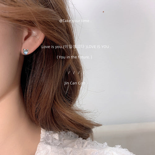 Silver-tone bow and blue-gray round cabochon studs shown worn on an ear.