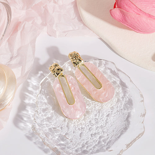 Pink oval drop earrings on clear glass dish with pink paper props