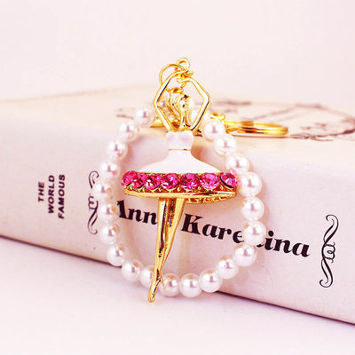 Front view of a gold-tone ballerina charm framed by white pearl-like beads on a book.