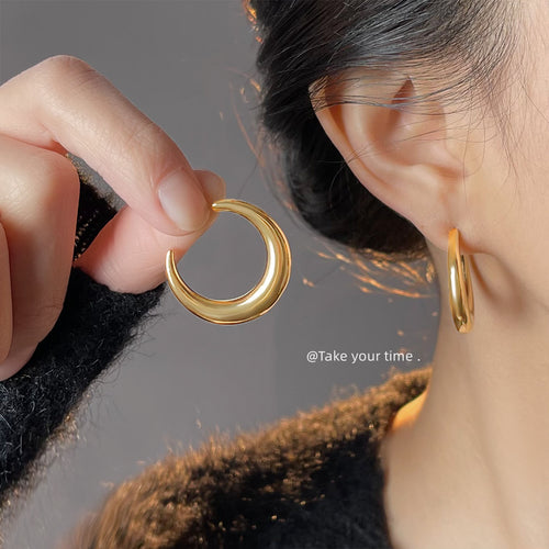Gold crescent hoop worn on ear while hand holds matching gold hoop