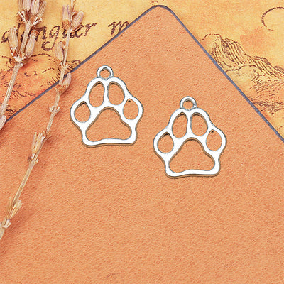 Pair of silver-tone openwork paw print charms on a tan card