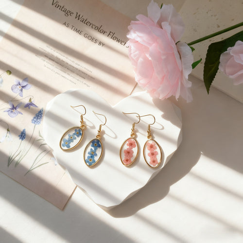 Two pairs pink and blue oval dried flower earrings on heart tray with peony