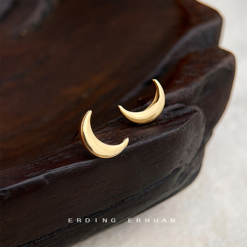 Gold crescent moon stud earrings on dark carved wood