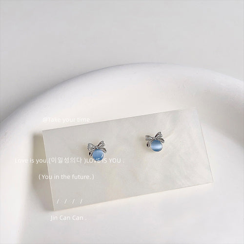 Silver-tone bow and blue-gray round cabochon studs on a pale card.