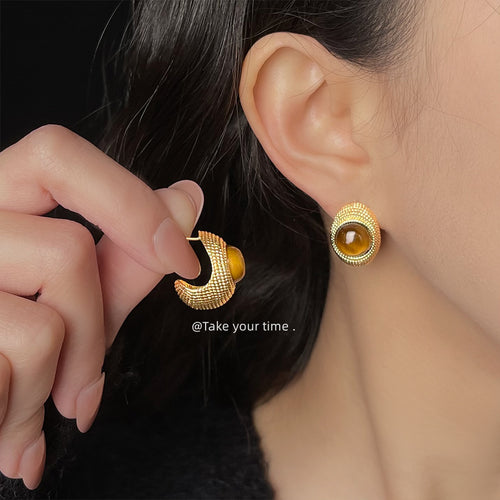 Model wearing gold textured tiger eye dome stud holding matching earring