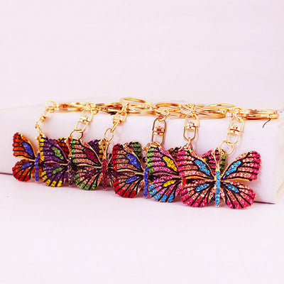 Six multicolor rhinestone butterfly keychains are lined up on a white display.