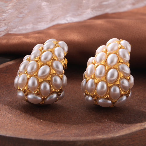 Pair of gold teardrop pearl cluster earrings on wood surface
