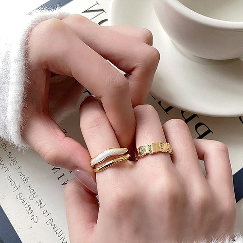 three unrelated gold-tone ring designs with white and geometric details shown worn in a styled second view