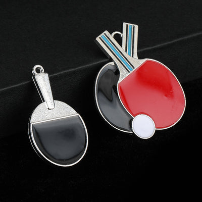 Small oval silver-tone table tennis paddle charm and a larger double paddle charm with red and black enamel side by side