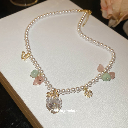 Close display of a pearl-like strand with pastel stone chips, small gold tone butterflies, and a clear heart drop