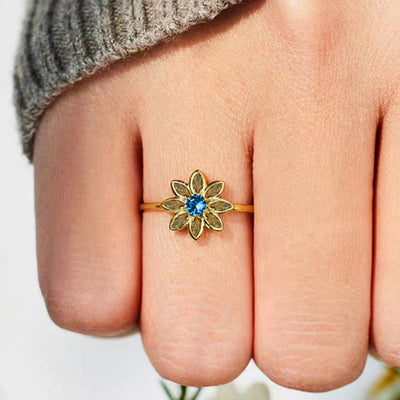 Front product view of gold tone flower ring with blue center and green petals