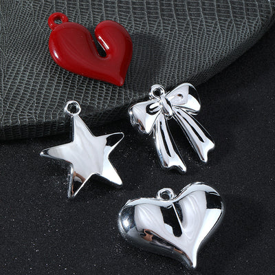Four silver-tone and red charms: a red heart, silver star, silver bow and silver heart on a gray textured surface
