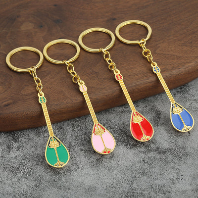 Four dombra keychains in green, pink, red and blue displayed on a wooden board.
