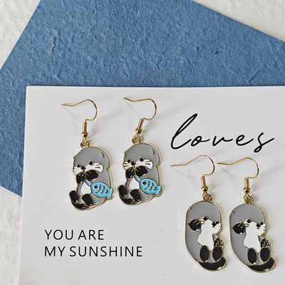 Two pairs of enamel gray sea lion earrings fish and reaching poses on white card