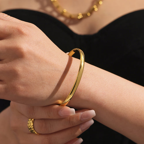 Single gold slim domed bangle worn against black clothing