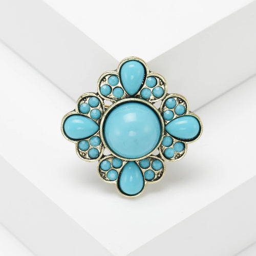 A round floral cluster of smooth colored cabochons and crystals shown in a styled display.