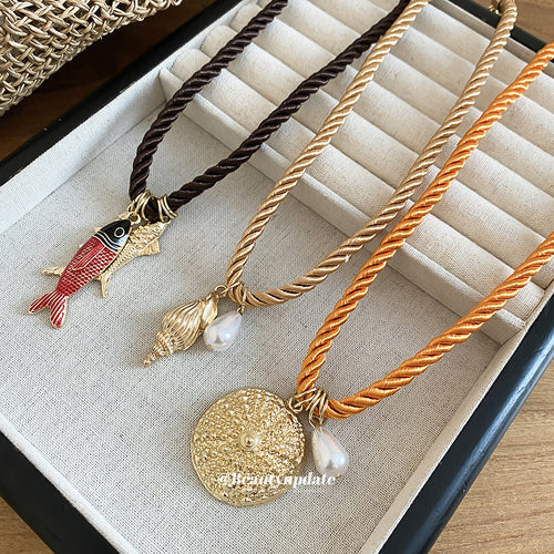 Close display of thick braided cords with fish, shell, or textured round pendants and small pearl-like accents