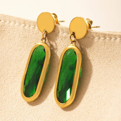 Pair of gold framed emerald green oval glass drop earrings on beige display